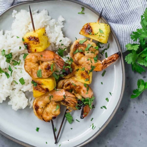 Overhead view of two grilled kabobs on a plate, with shrimp and fresh pineapple. They are served with white rice and sprinkled with fresh cilantro.