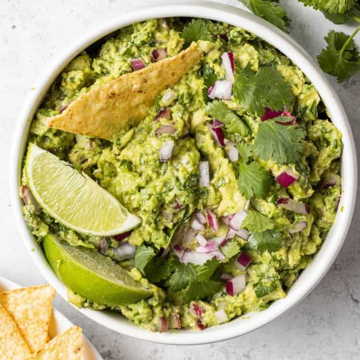 Round white bowl filled with guacamole, one chip dipped in.