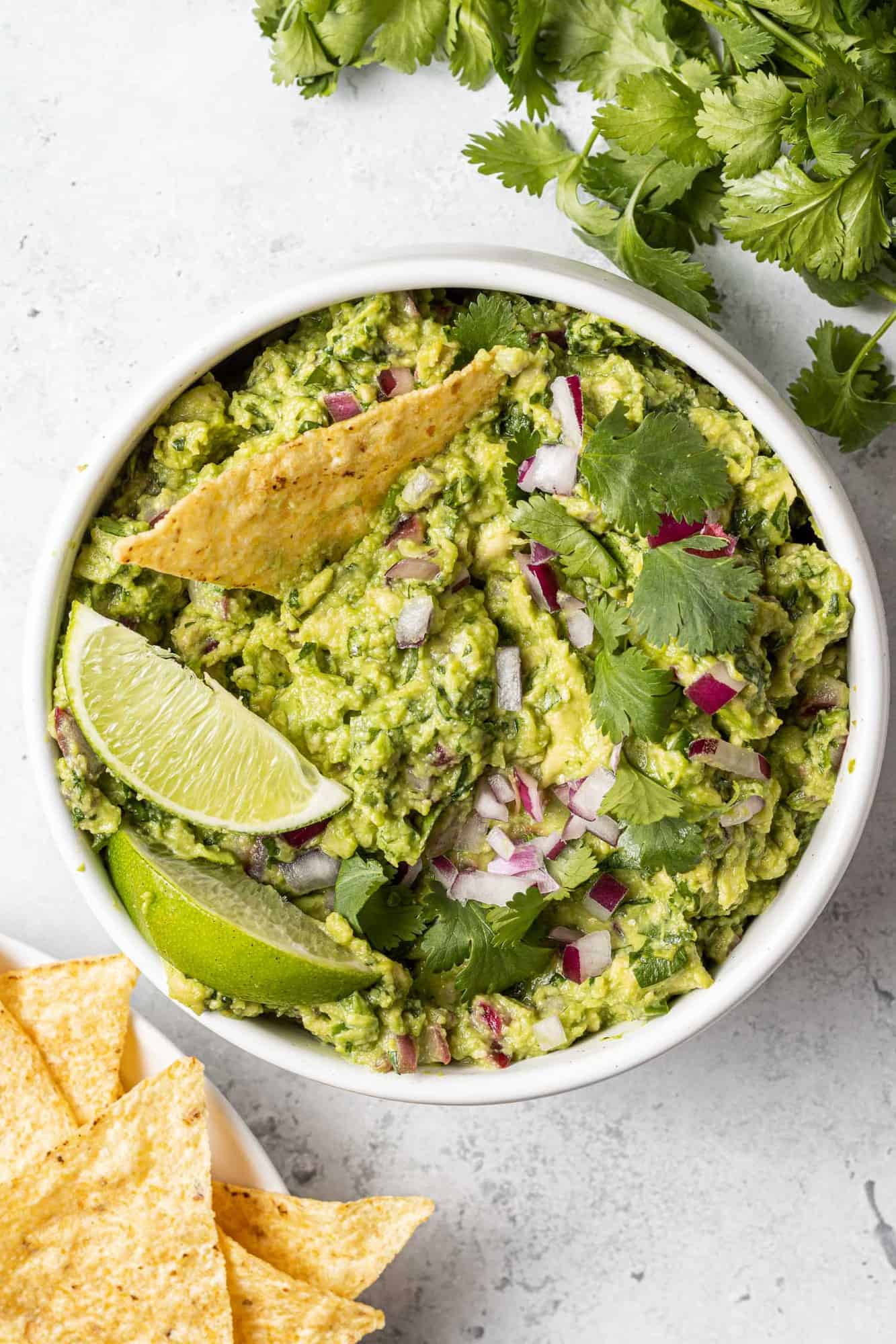 Overhead view of a white bowl of guacamole with a chip dipped in and lime wedges on top.