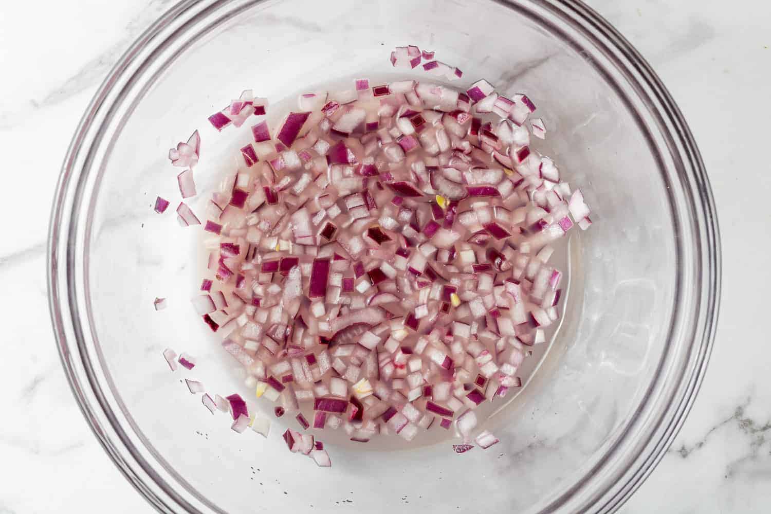 Onions in lime juice in a clear glass bowl.