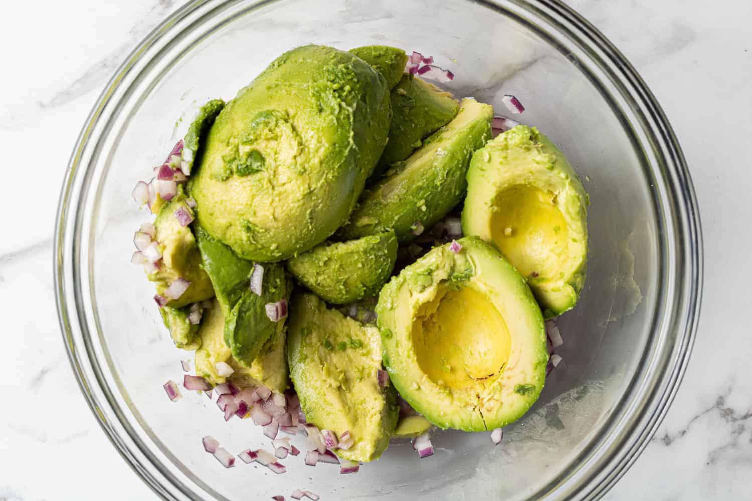 Peeled avocado halves in a bowl with red onions.