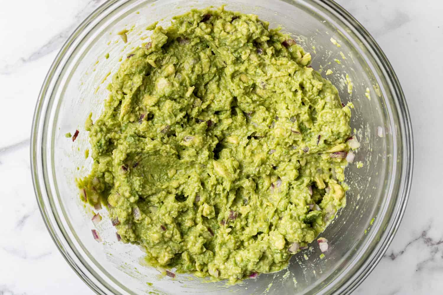 Mashed avocado in a clear glass bowl.