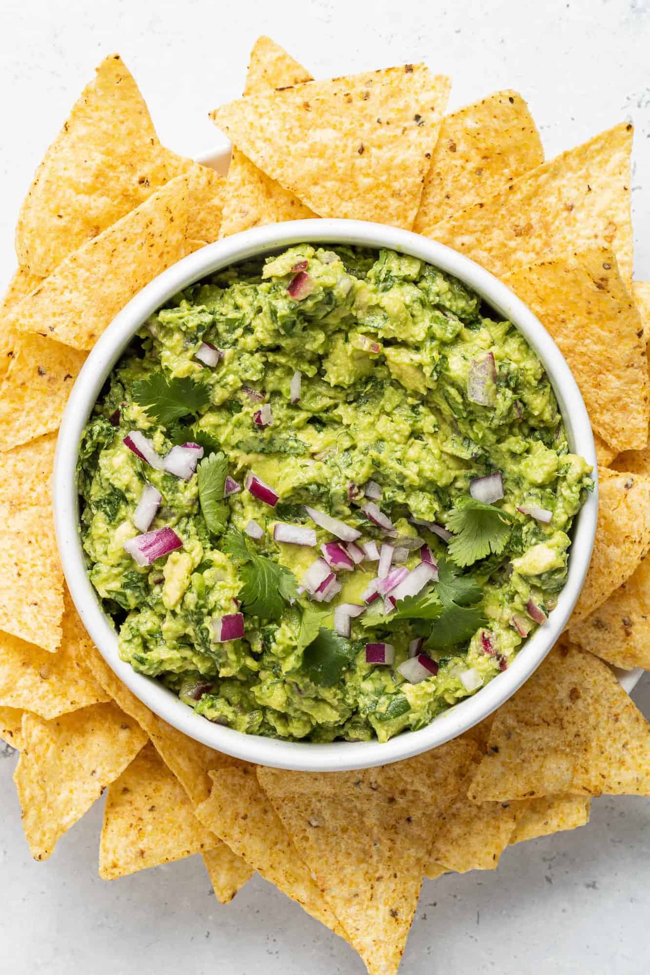 Guacamole in a white bowl surrounded by chips.