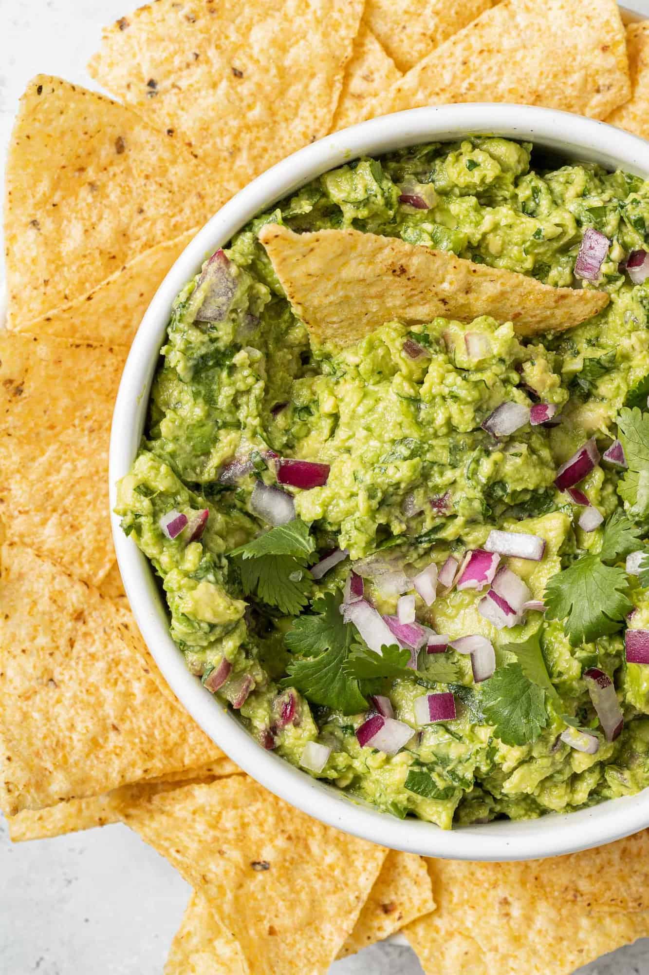 Close up of a bowl of homemade guacamole surrounded by tortilla chips.