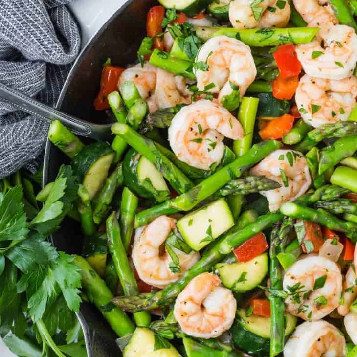 Overhead view of shrimp and vegetables in a white skillet.