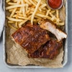 Barbecued ribs on a tray with fries and ketchup.