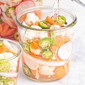 Vegetables in a jar with liquid being poured into it.