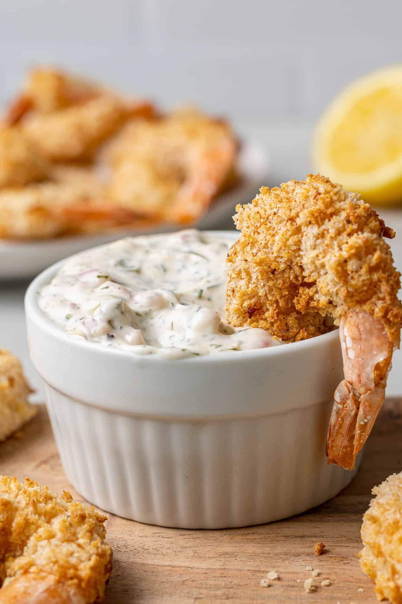 Breaded shrimp hanging over edge of a bowl of tartar sauce.