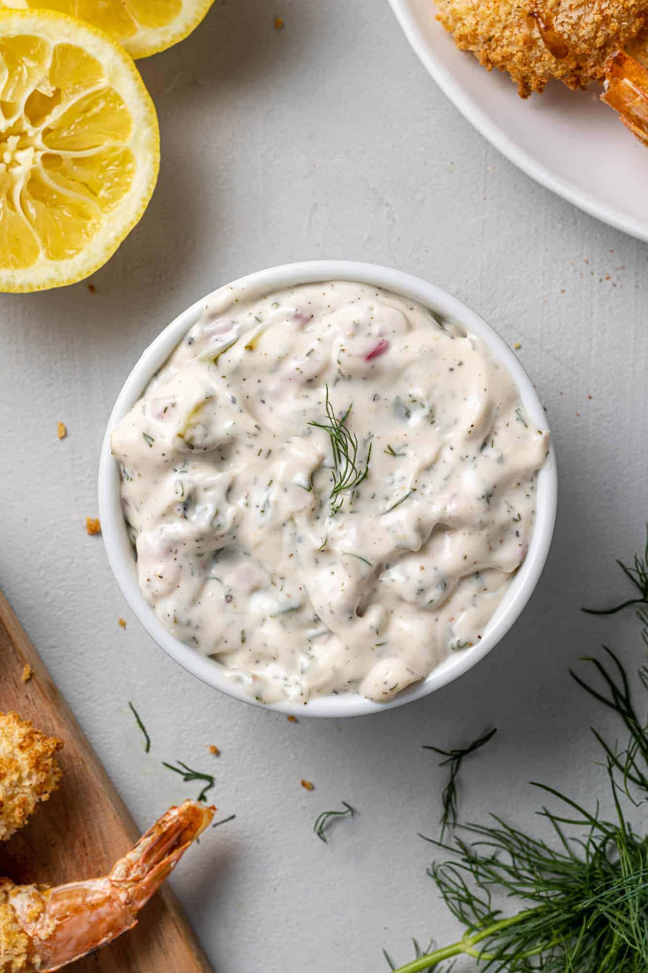 White creamy sauce surrounded by breaded shrimp, fresh dill, and lemon halves.