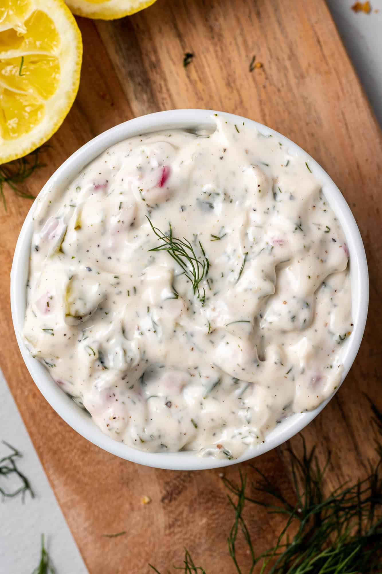 Overhead view of a creamy white sauce with dill in a white bowl on a wooden surface.