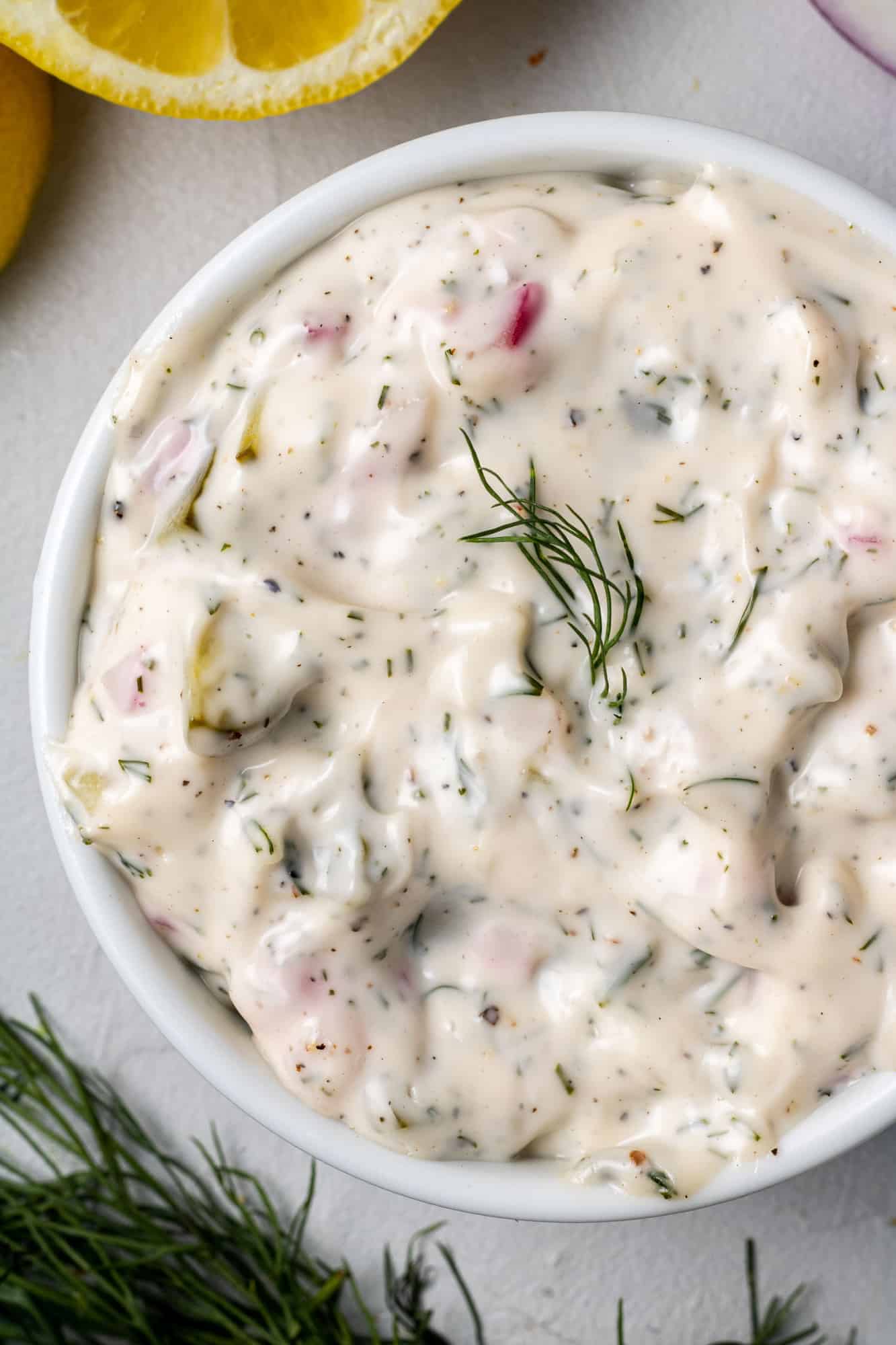 Overhead view of homemade tartar sauce in a round white bowl garnished with fresh dill.