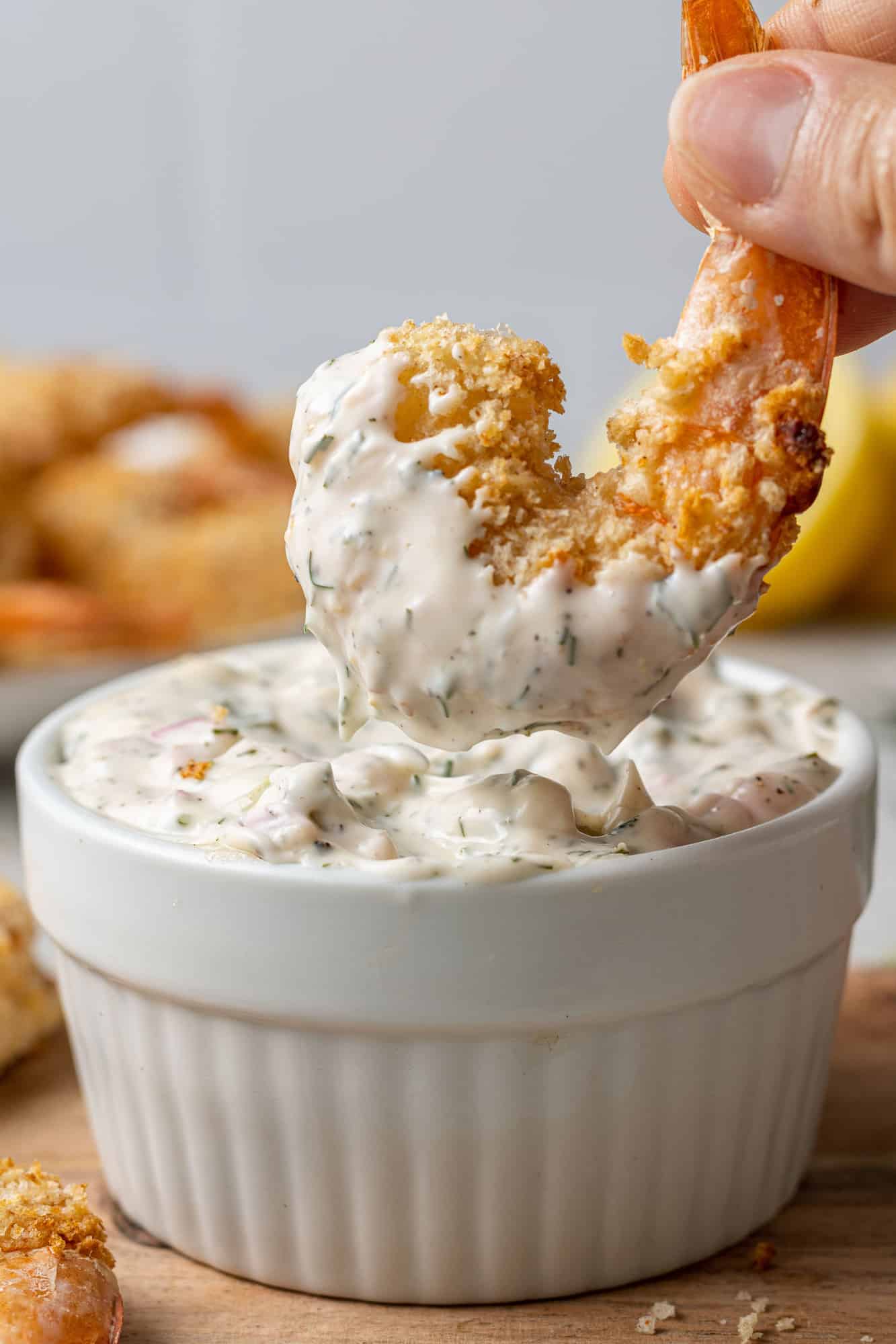 Breaded shrimp being held in a hand and dipped in tartar sauce.