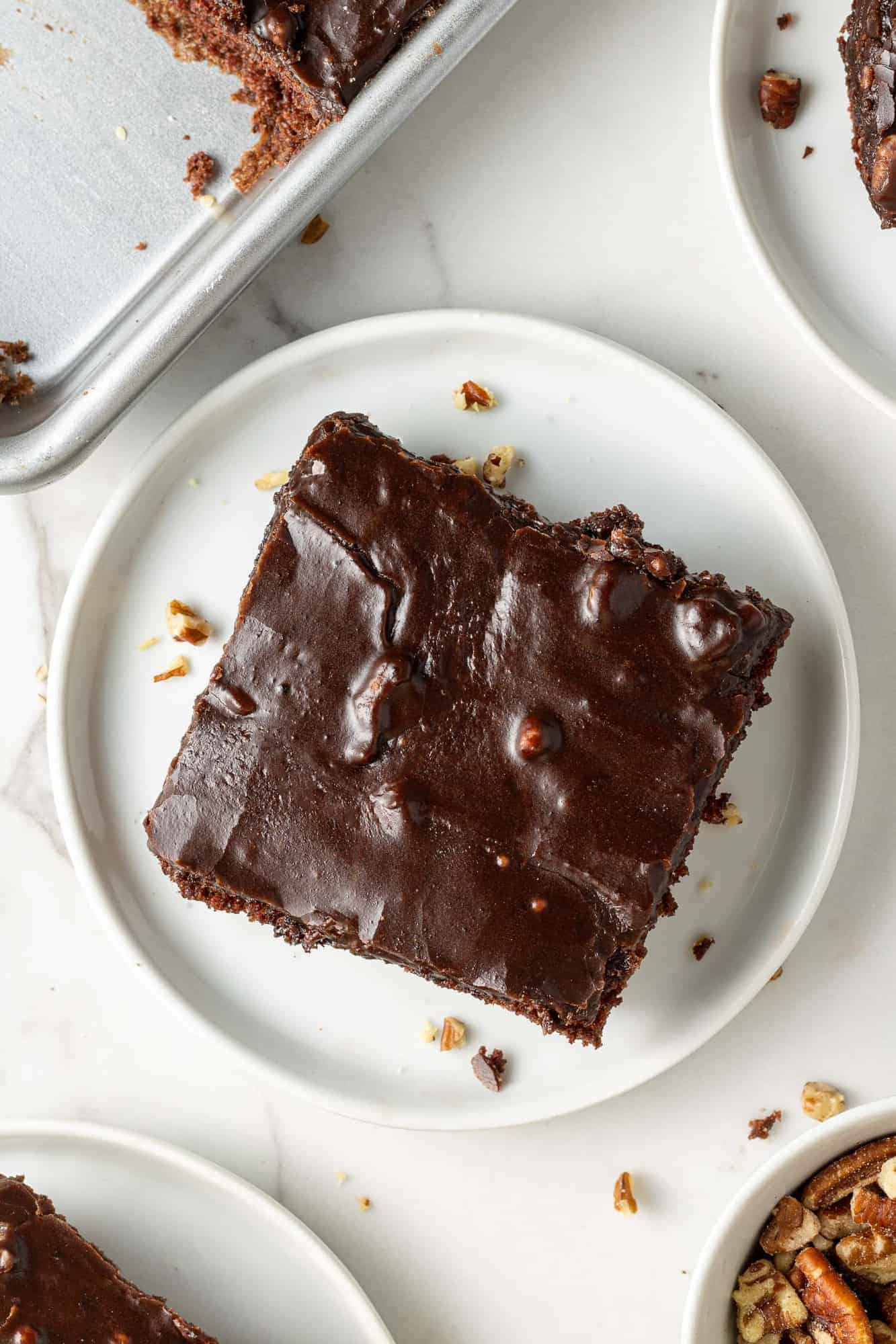 Overhead view of square piece of chocolate cake with thin frosting, on a round white plate.