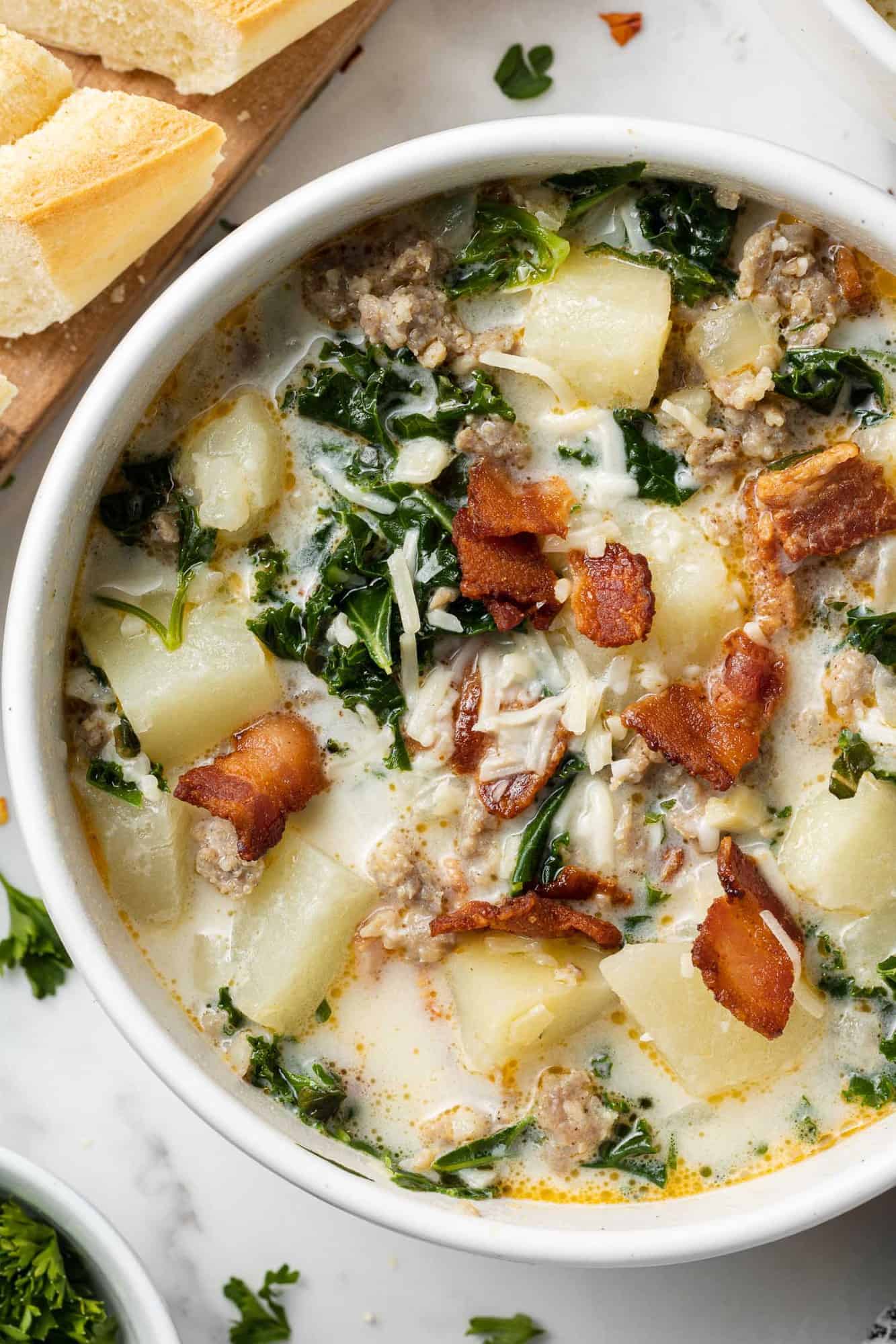 Overhead view of zuppa toscana soup in a white bowl garnished with crispy bacon.