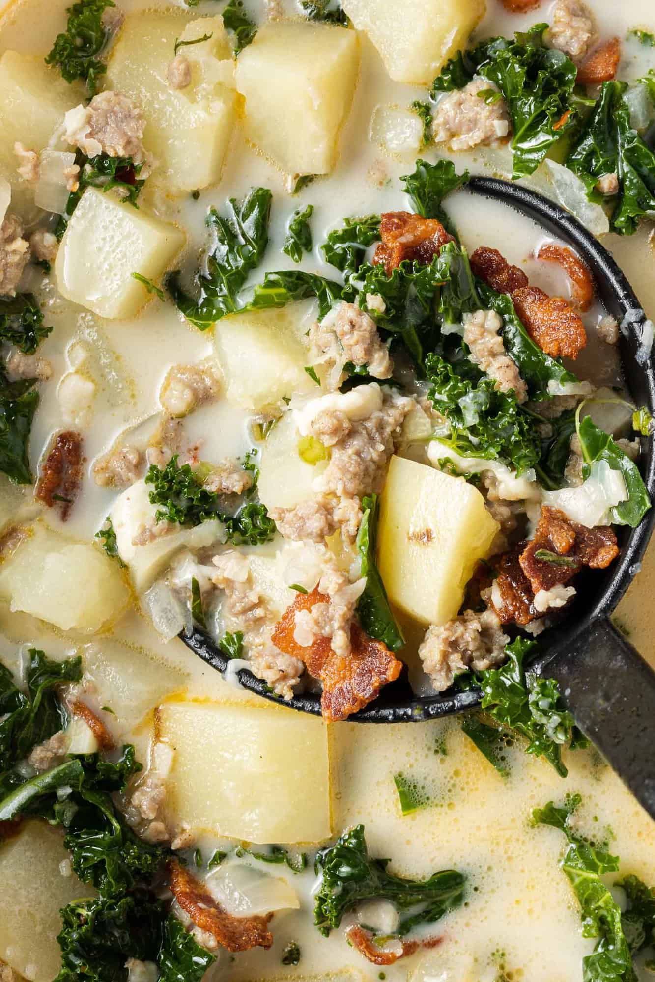 Creamy soup with kale, sausage, and potatoes shown in a ladle.