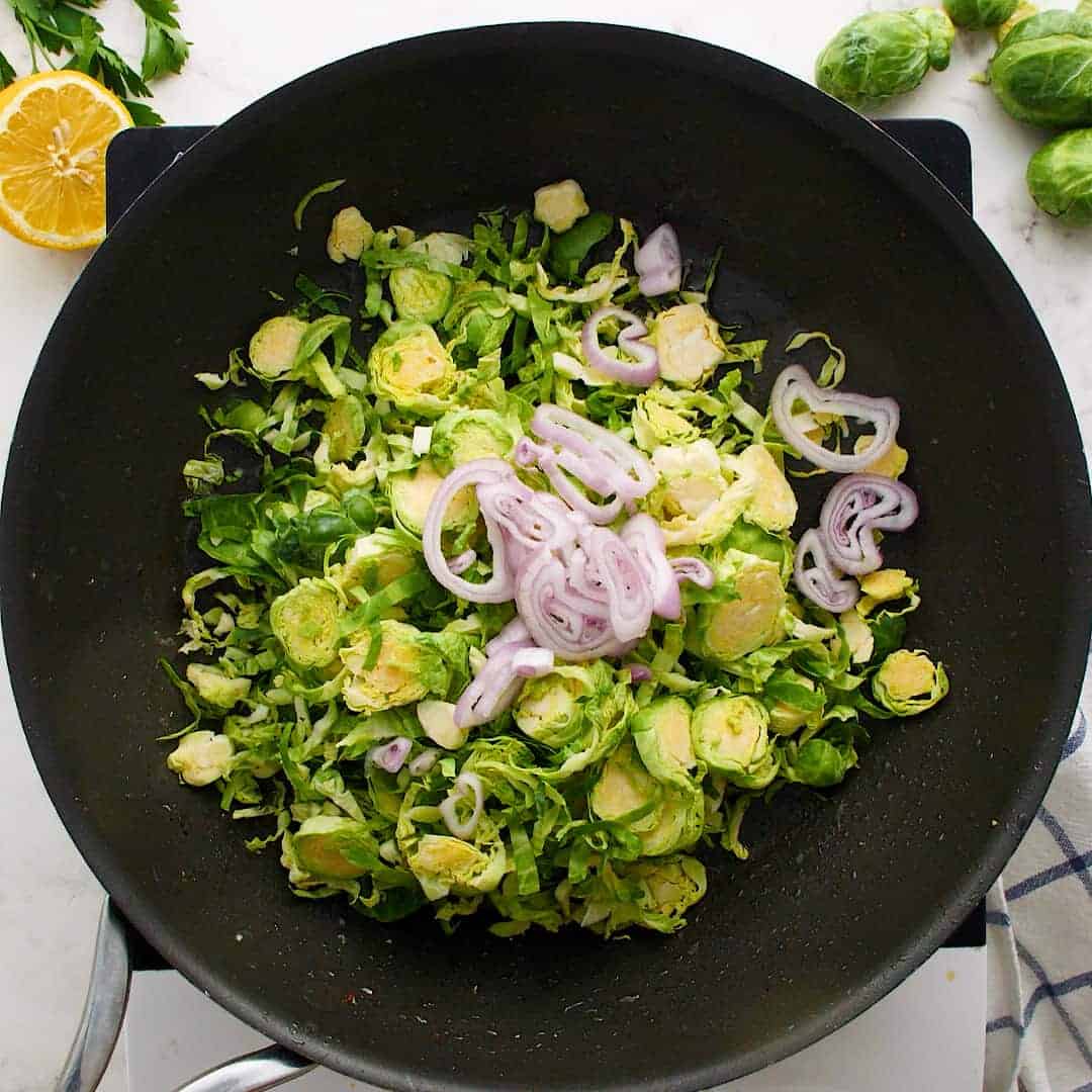 Brussels sprouts and shallots in a black frying pan.