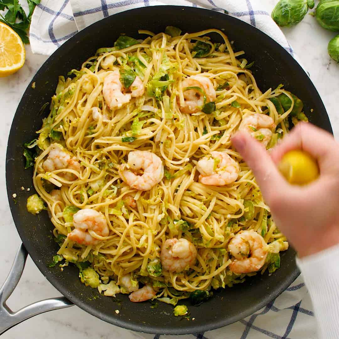 Lemon being squeezed over pasta with Brussels sprouts.