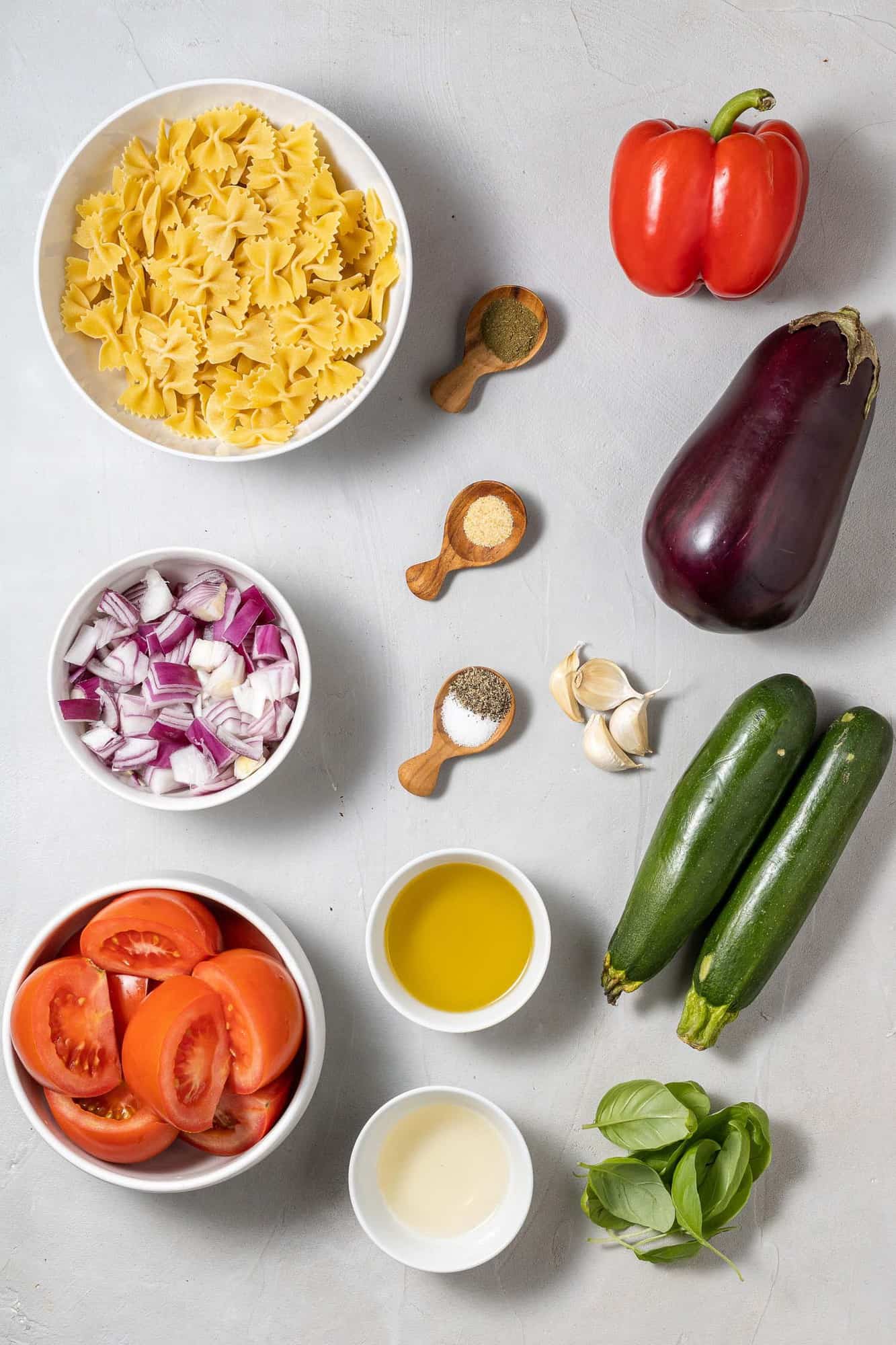 Fresh vegetables, cooked pasta, and dressing ingredients on a gray background.