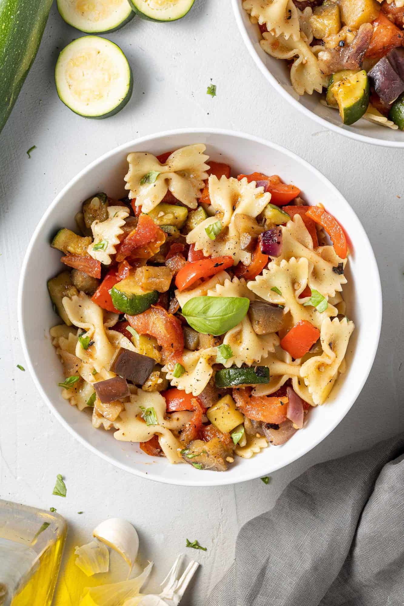 Round white bowl with bowtie pasta, grilled vegetables, fresh basil.