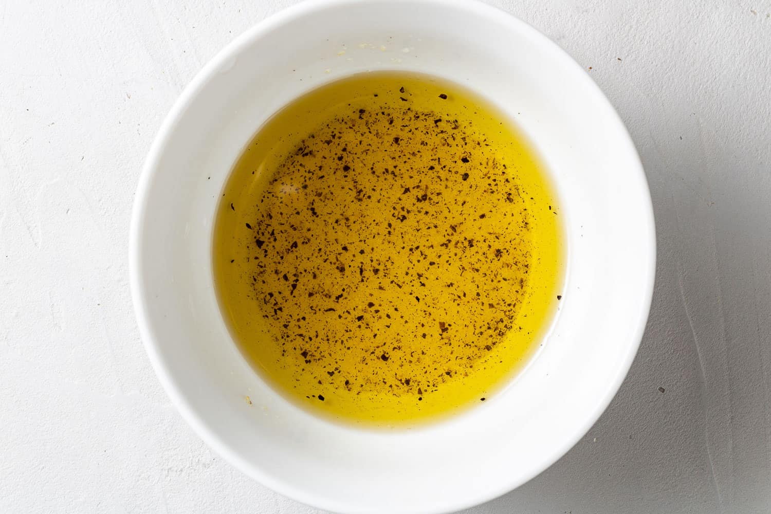 Olive oil based salad dressing in a small white bowl.