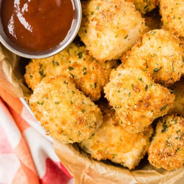 Air fryer chicken nuggets in a basket, shot from above. BBQ sauce also pictured.