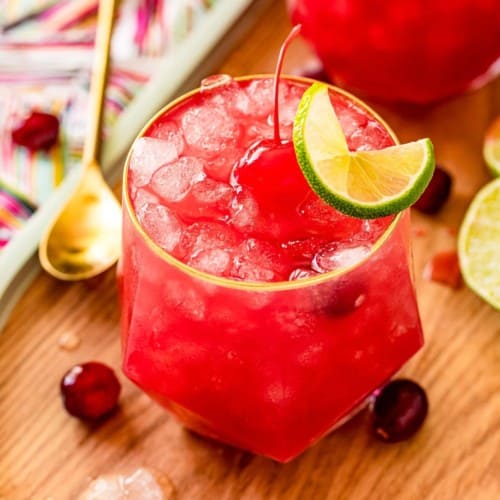 Bright red cocktail garnished with a cherry and a lime wheel.