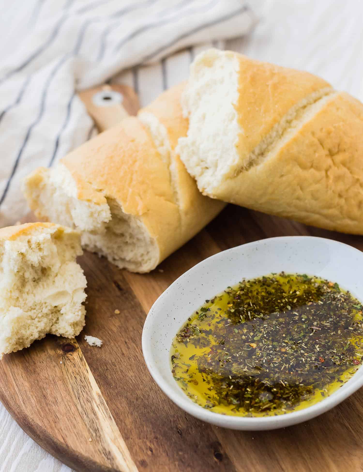 Round wooden cutting board with a small bowl of olive oil and seasonings, and a loaf of bread.