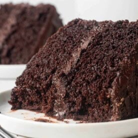 Slice of chocolate layer cake on a round white plate, with a bite removed.
