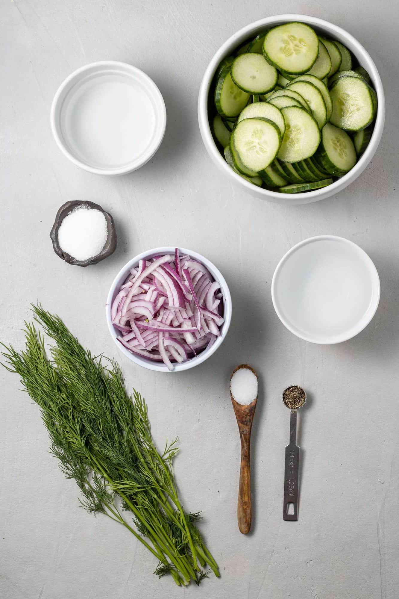 Overhead view of ingredients needed for recipe: cucumber, dill, onion, vinegar, salt, pepper, sugar.