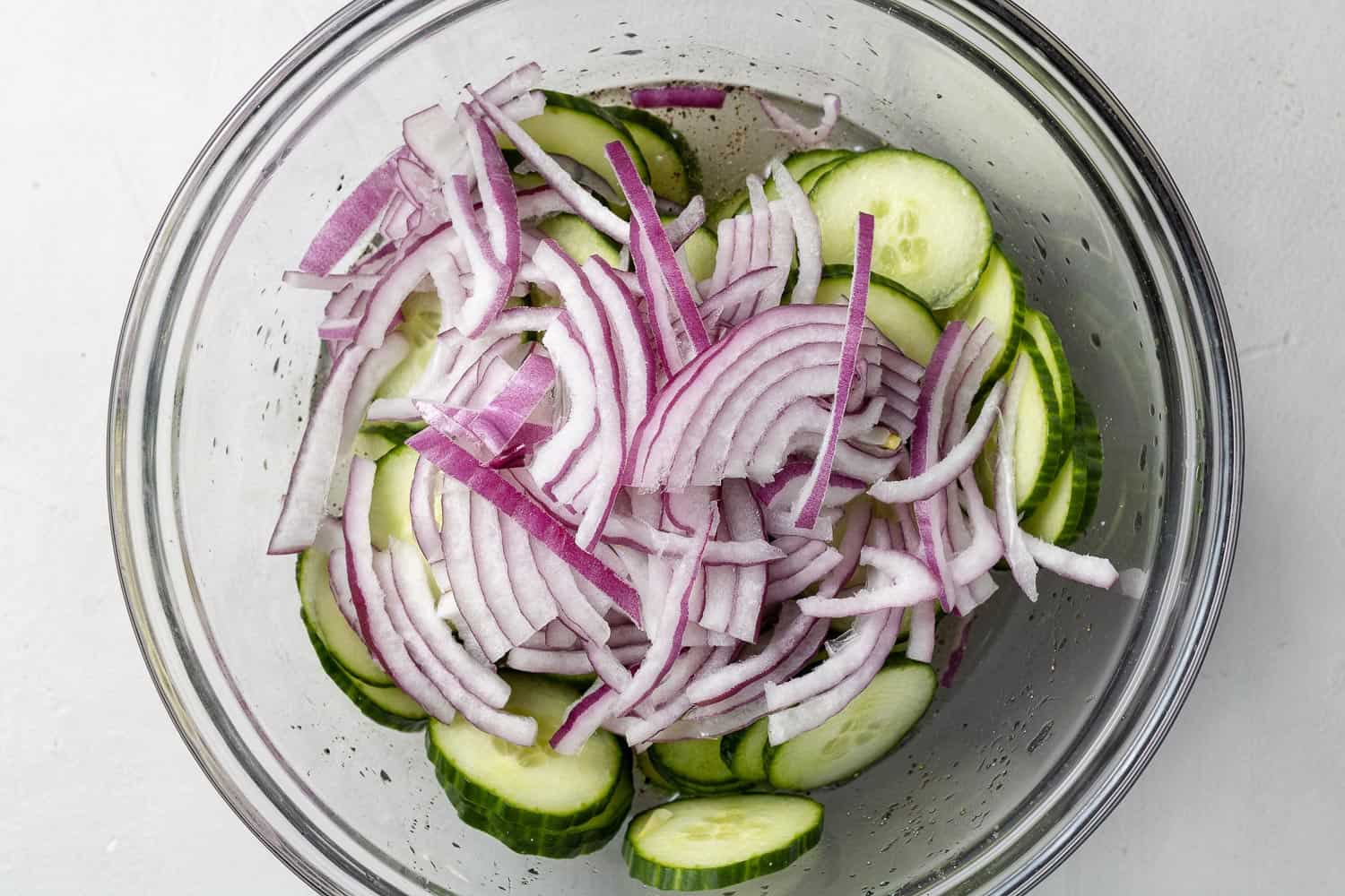 Cucumbers and sliced onions in a large glass mixing bowl.