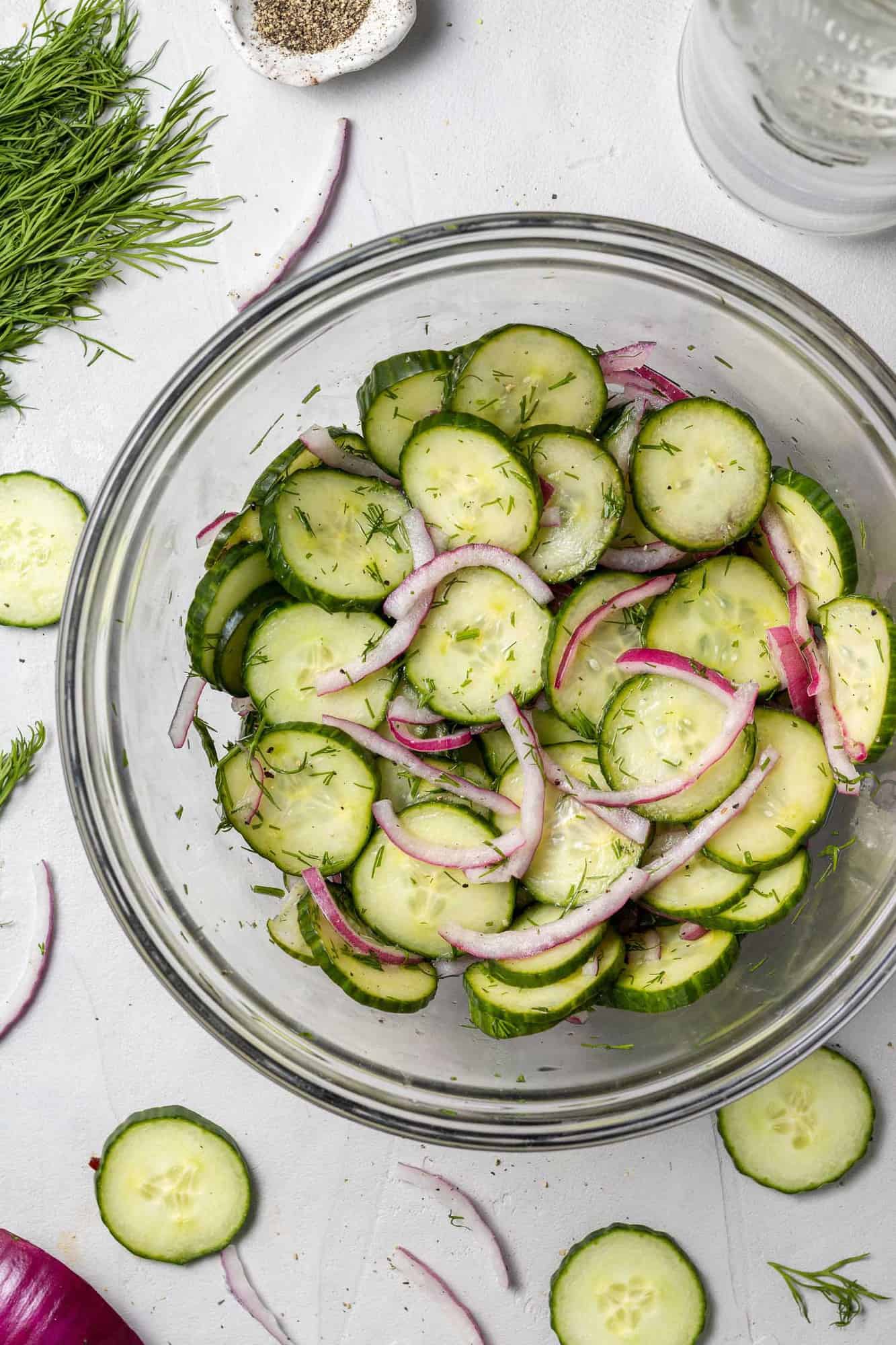 Overhead view of sliced cucumbers and onions in a clear glass bowl.