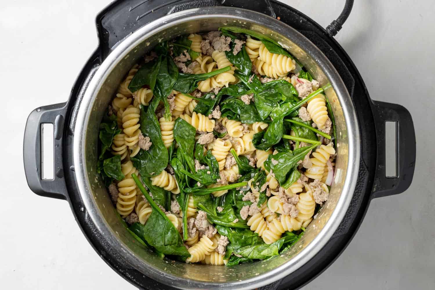 Spinach on top of ground chicken and pasta in an instant pot.