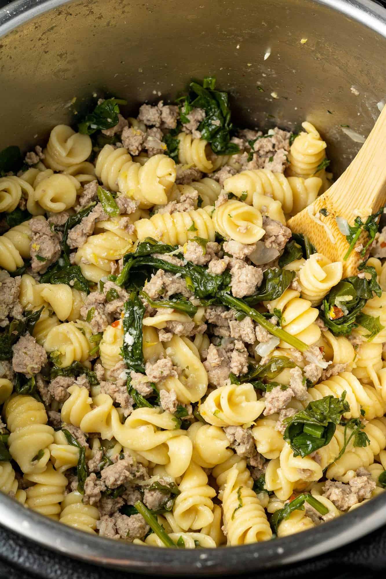 Instant pot filled with pasta, spinach, ground chicken, and a wooden spoon.