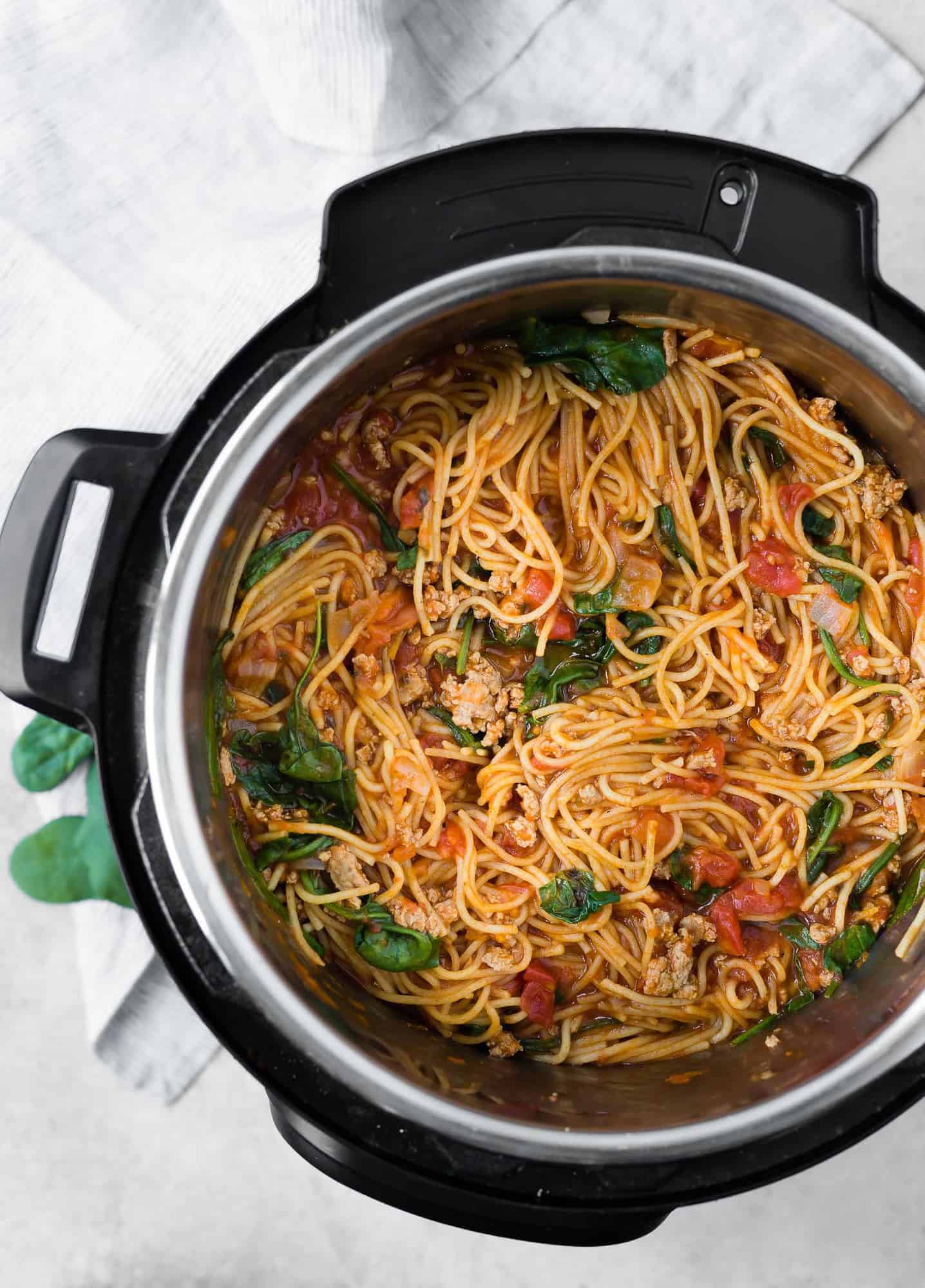 Overhead view of spaghetti in an instant pot, with a meat sauce and spinach.