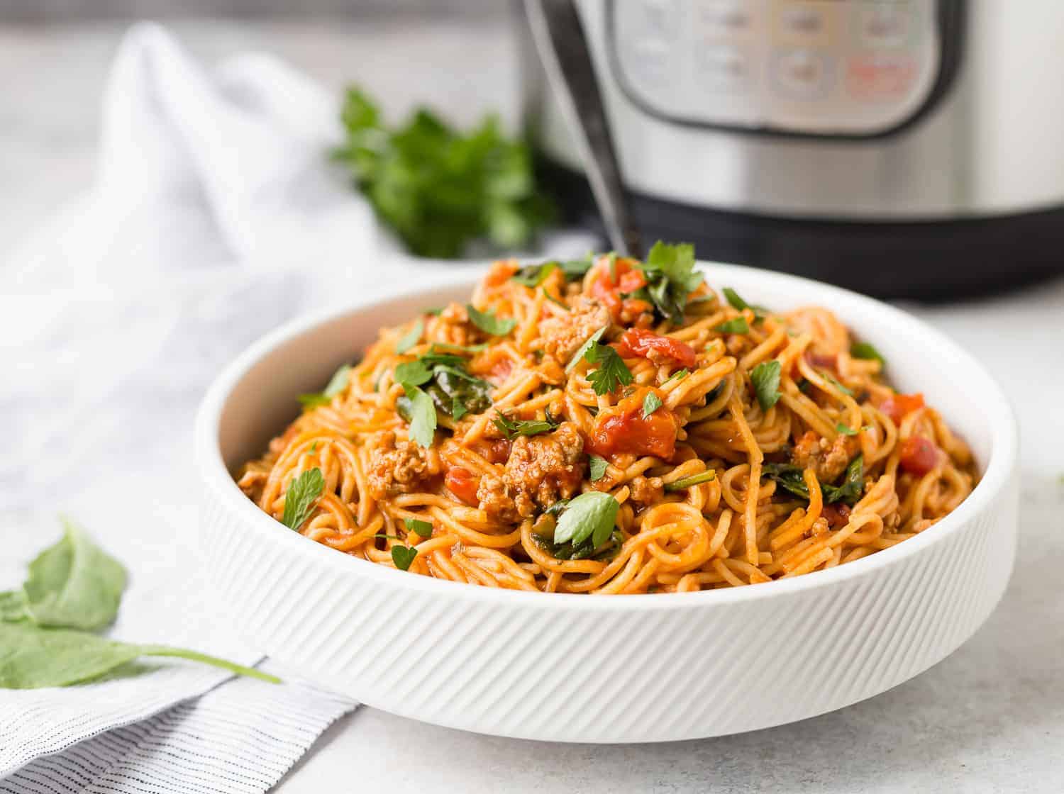 A bowl of spaghetti with a black spoon in front of an instant pot.