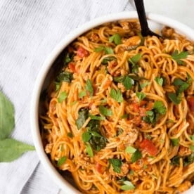 Overhead view of spaghetti and meat sauce in a white bowl, sprinkled with parsley.