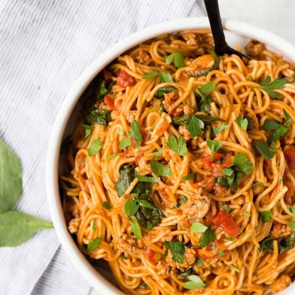 Overhead view of spaghetti and meat sauce in a white bowl, sprinkled with parsley.