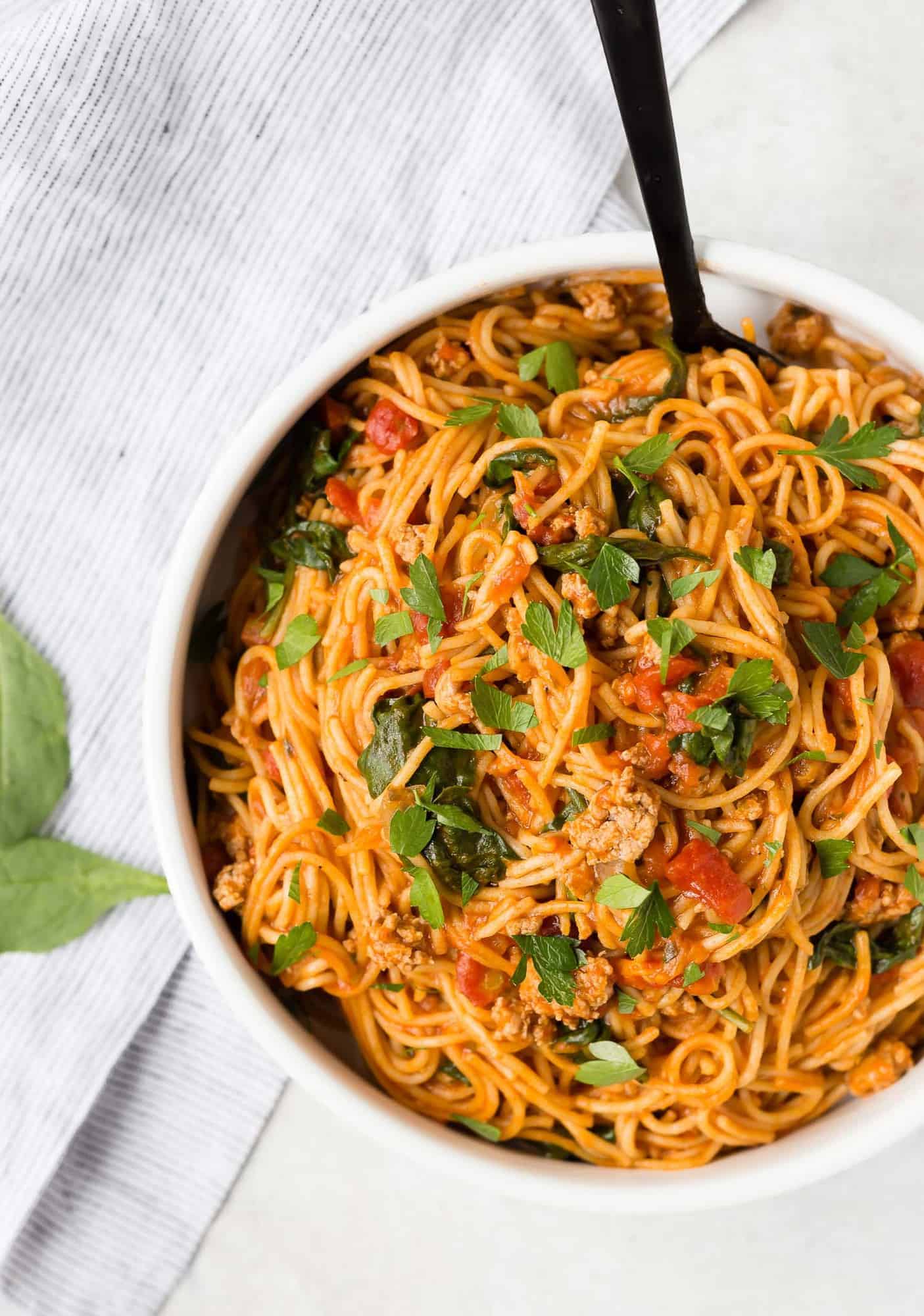 Spaghetti in a white bowl with a black spoon.