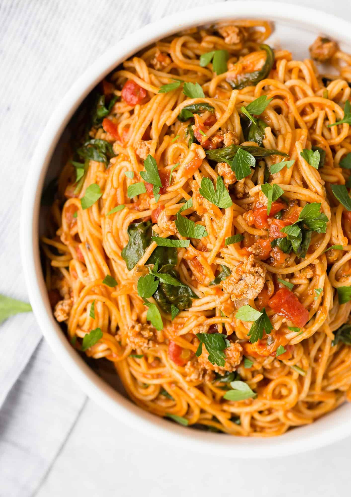 Overhead view of spaghetti and meat sauce in a white bowl, sprinkled with parsley.