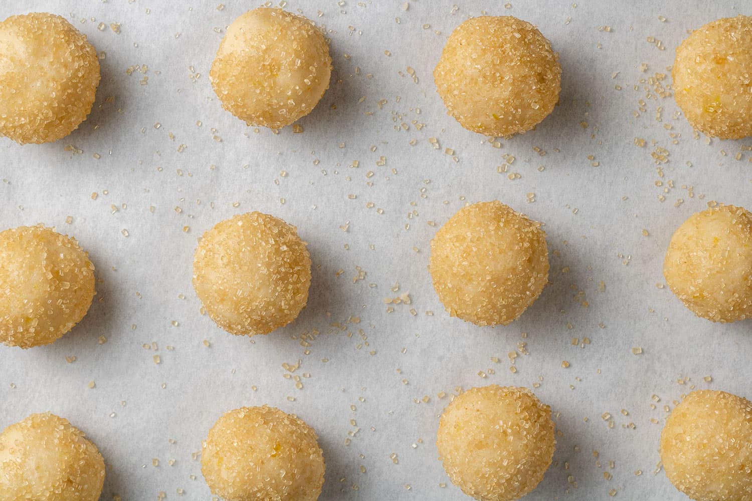 Unbaked lemon cookie dough balls on a parchment paper lined baking sheet.