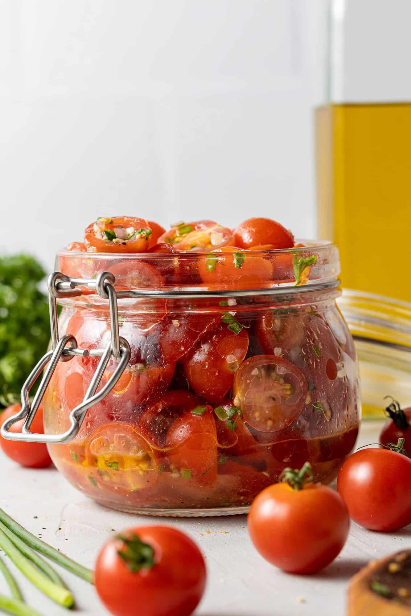 Tomatoes with olive oil and herbs in a small glass jar. Fresh tomatoes in the foreground.