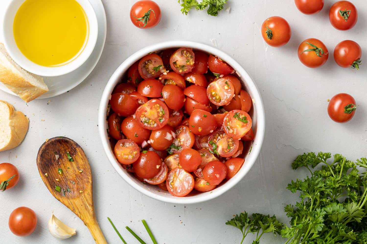 Tomatoes, surrounded with fresh herbs, oil, and a wooden spoon.