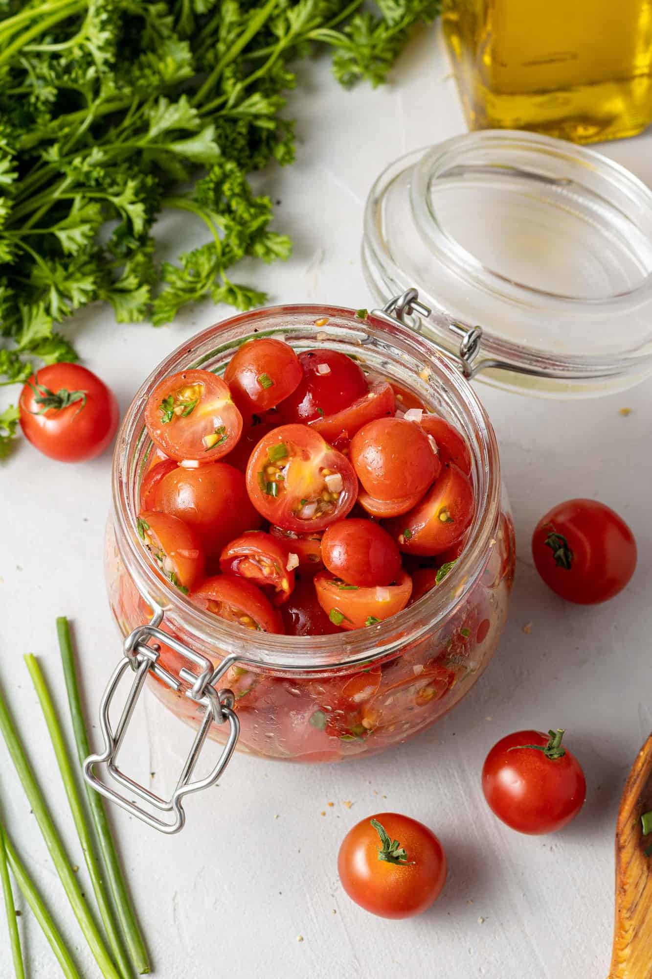 Tomatoes in a jar surrounded by fresh herbs.