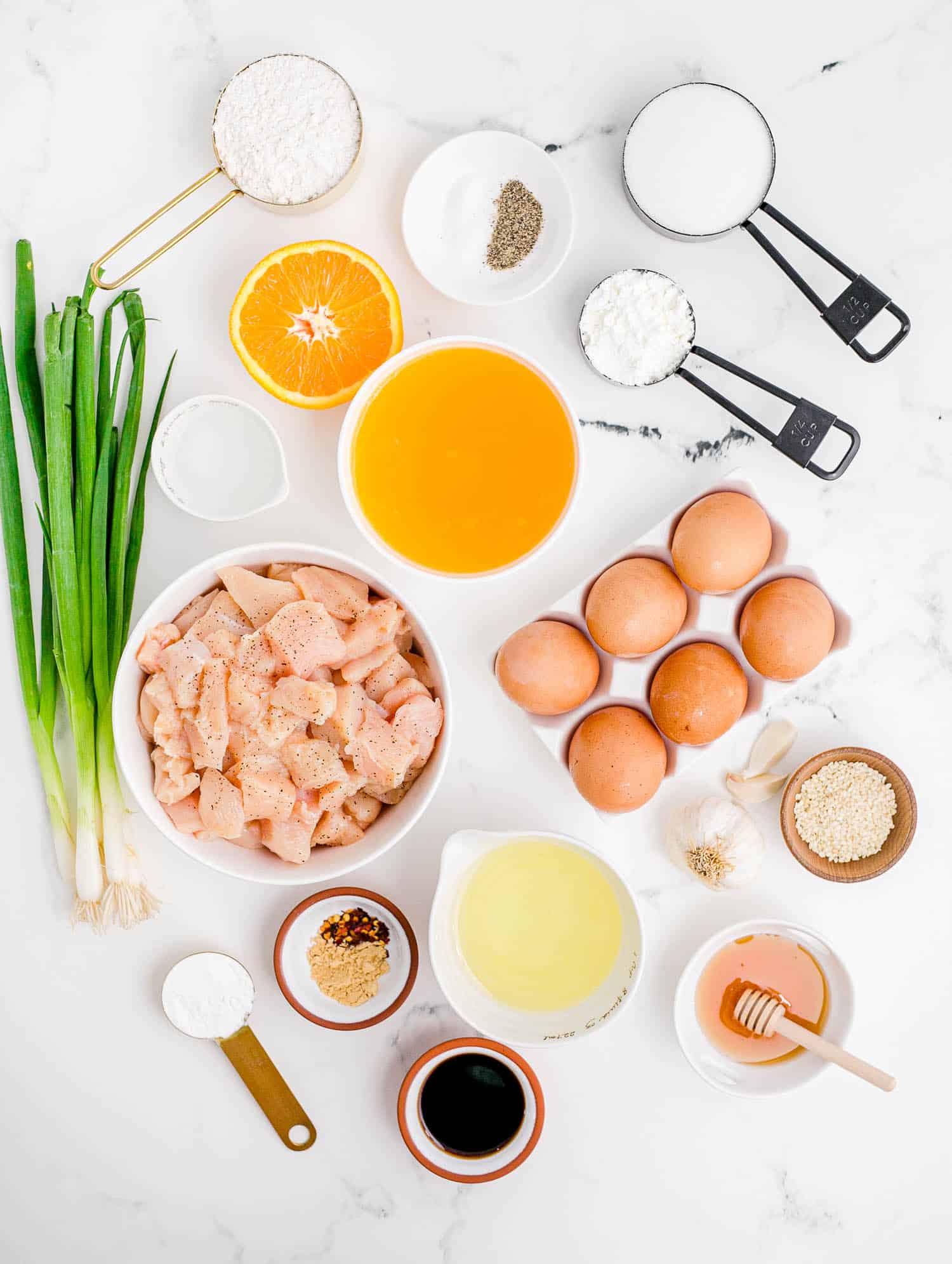 Overhead view of ingredients needed for recipe including chicken, eggs, orange juice, and green onion.