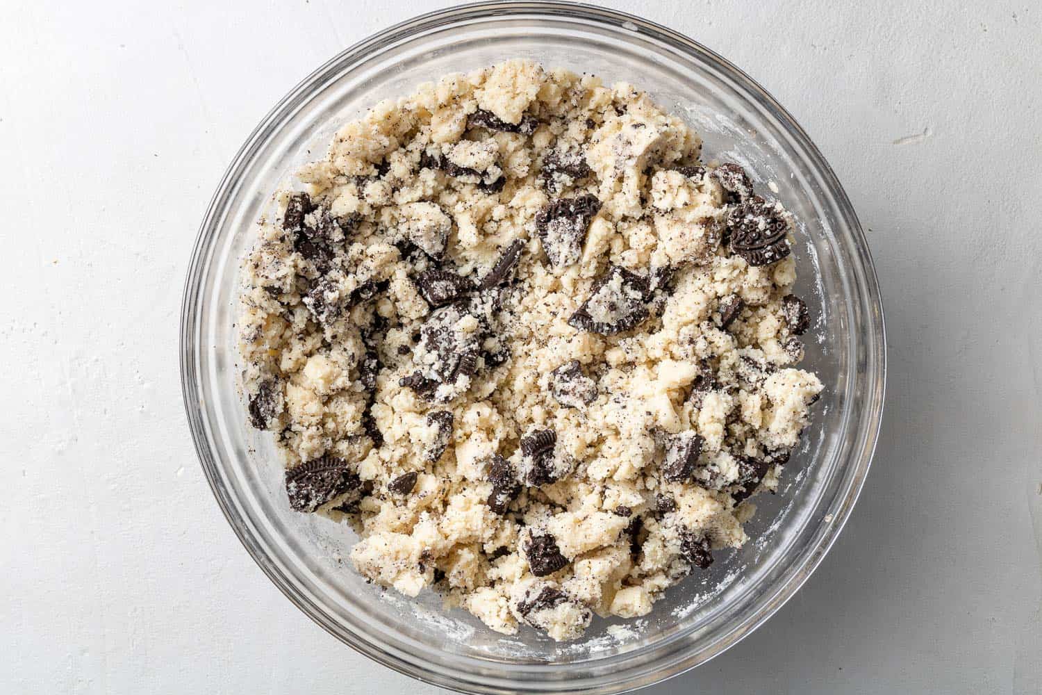 Cookie dough with oreo pieces mixed in, in a glass mixing bowl.