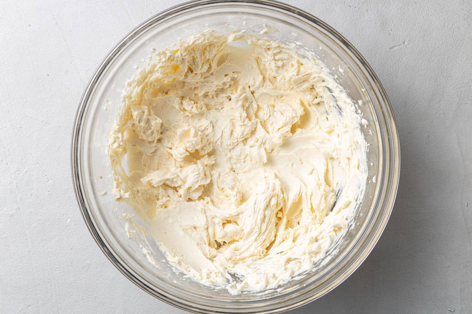Butter and cream cheese creamed together in a glass mixing bowl.