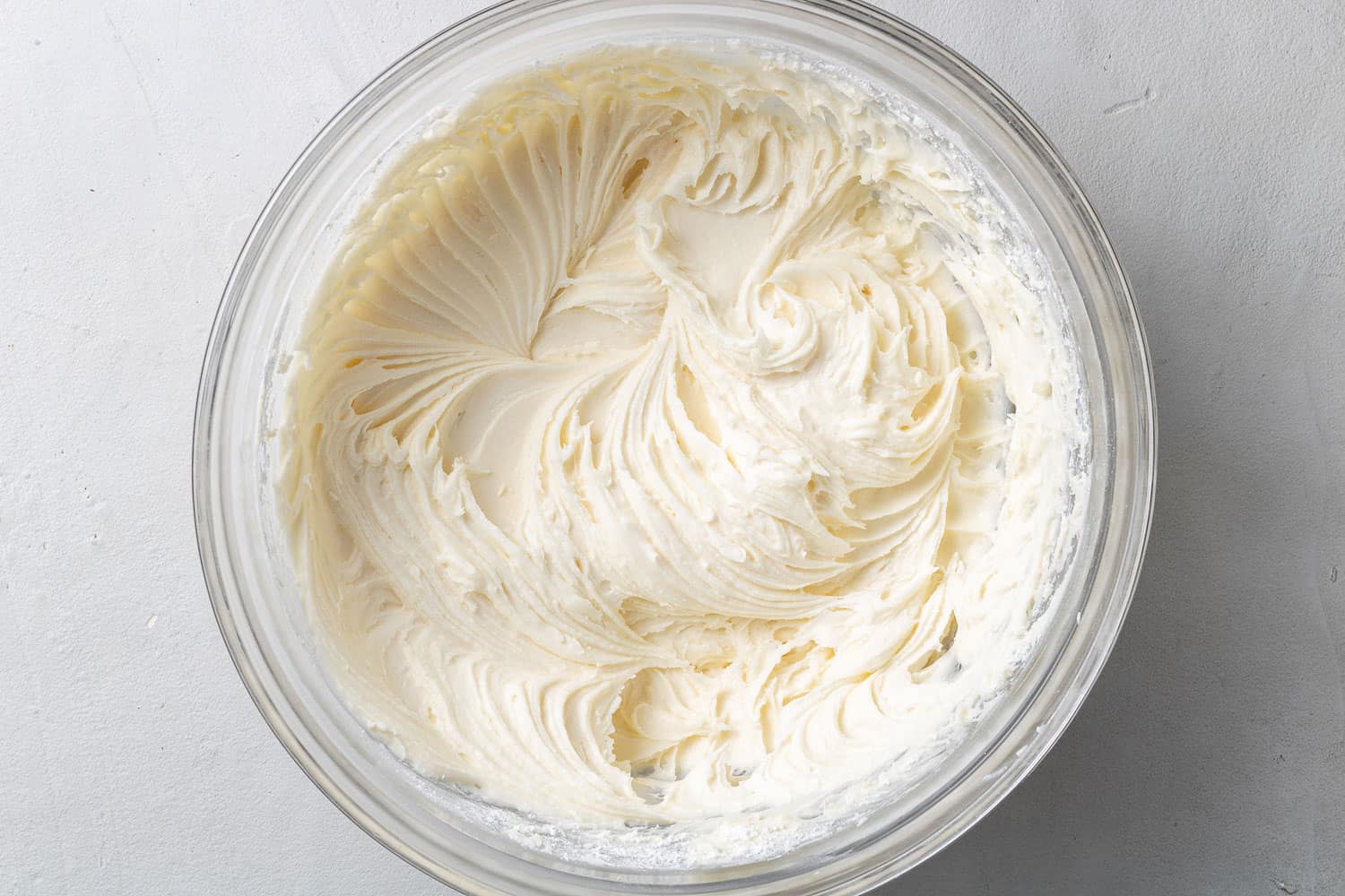 Cream cheese frosting in a clear glass mixing bowl.