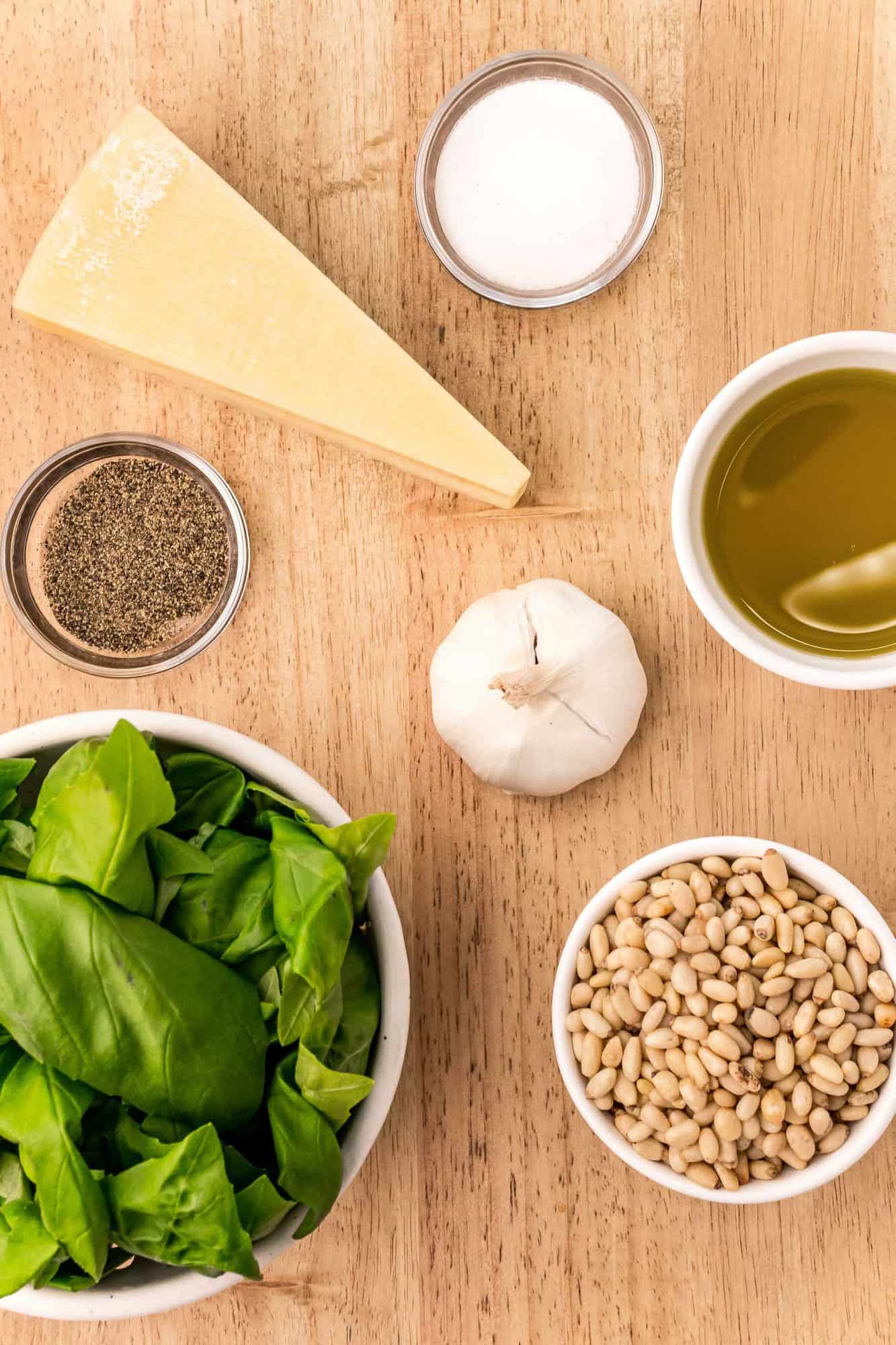 Overhead view of ingredients needed for recipe: basil, cheese, pine nuts, olive oil and garlic.