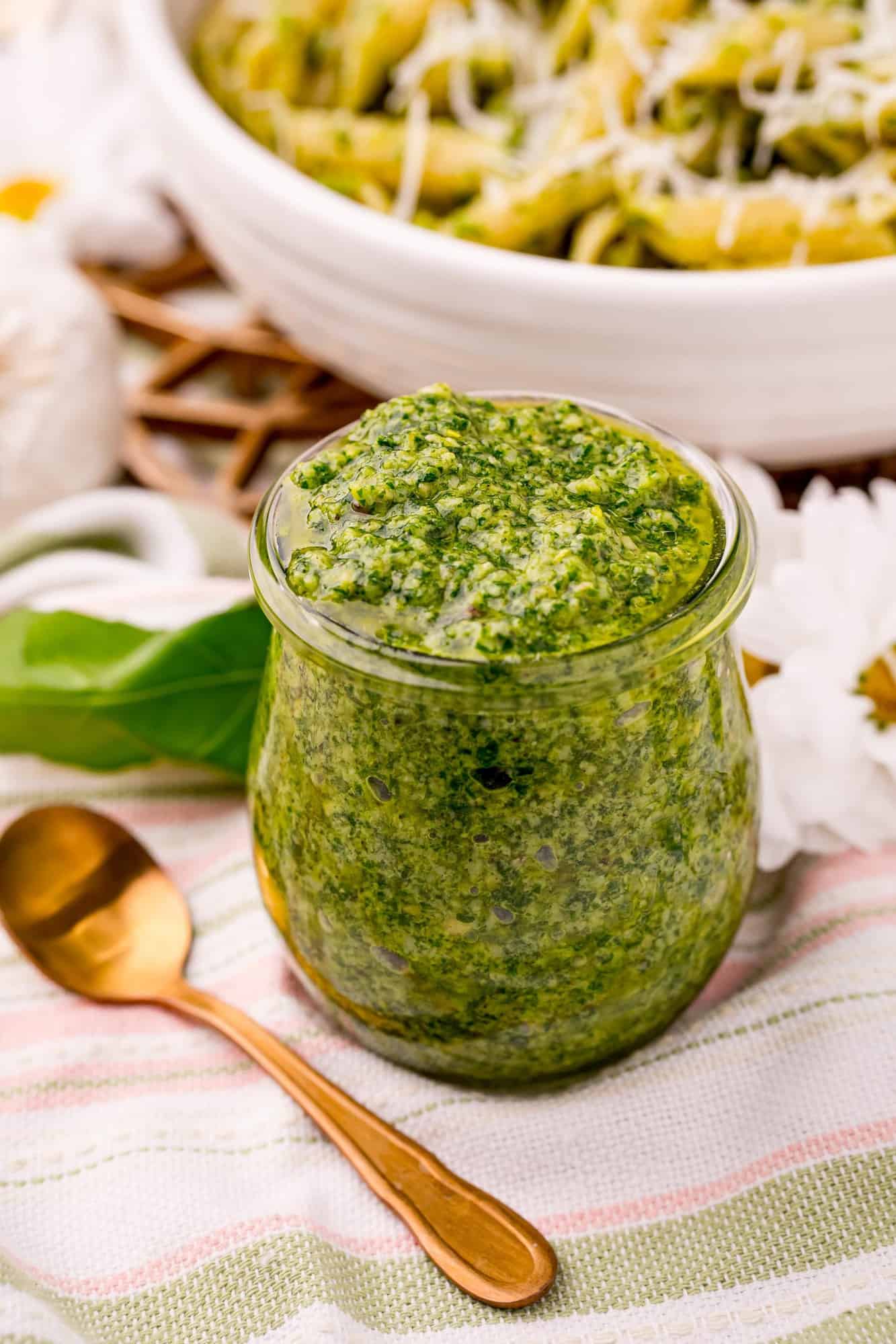 Pesto in a jar in front of a bowl of pasta.