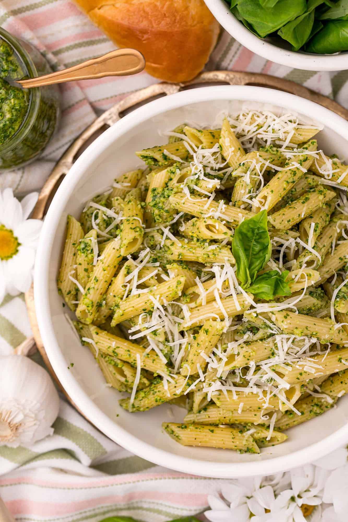 Overhead view of penne pasta in a white bowl, coated with pesto.